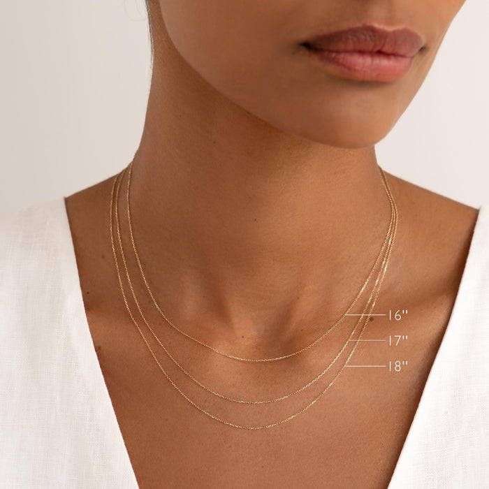 Close-up of a woman wearing layered 14k gold cable chain necklaces in 16, 17, and 18 inch lengths with a white linen top