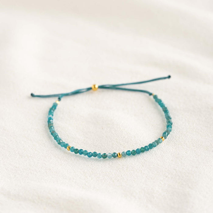 Apatite Bracelet featuring dainty blue beads with gold vermeil accents on an adjustable cord laid flat on a light background