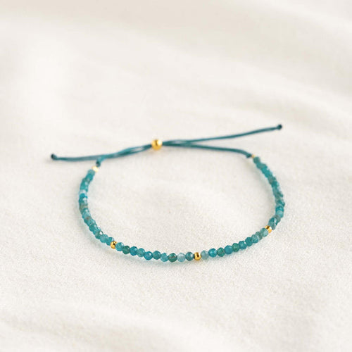 Apatite Bracelet featuring dainty blue beads with gold vermeil accents on an adjustable cord laid flat on a light background