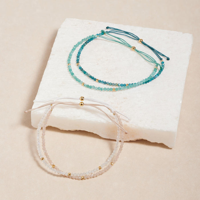 Two dainty Apatite Bracelets with gold vermeil bead accents displayed on a light textured stone block