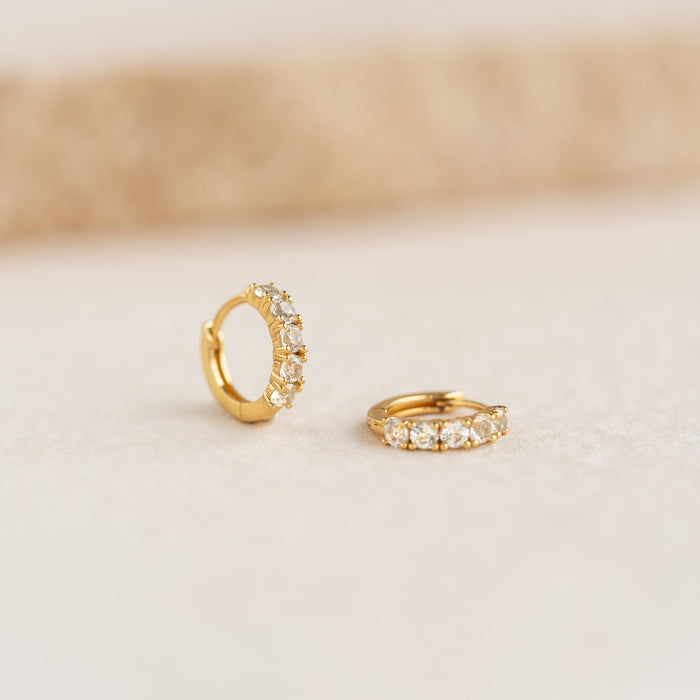 Close-up of April Birthstone Huggie Earrings - White Topaz with gold vermeil setting on a neutral surface