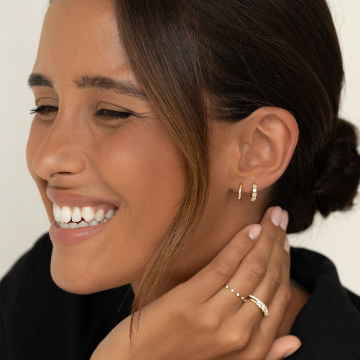 Close-up of a smiling woman wearing April Birthstone Huggie Earrings - White Topaz with gold rings on her fingers