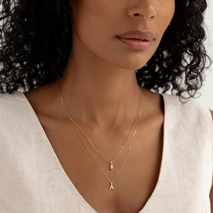 Close-up of woman wearing the April Birthstone Pendant 14k Gold - White Topaz layered with a gold letter A necklace