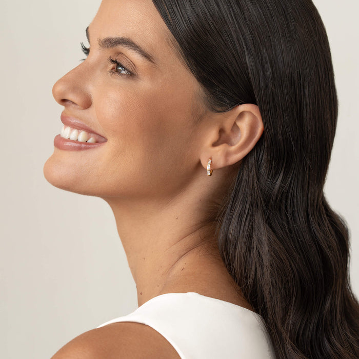 Smiling woman in profile wearing a small Gold Vermeil earring set with baguette-cut gemstone, shown against a soft neutral background with dark hair styled behind the ear.
