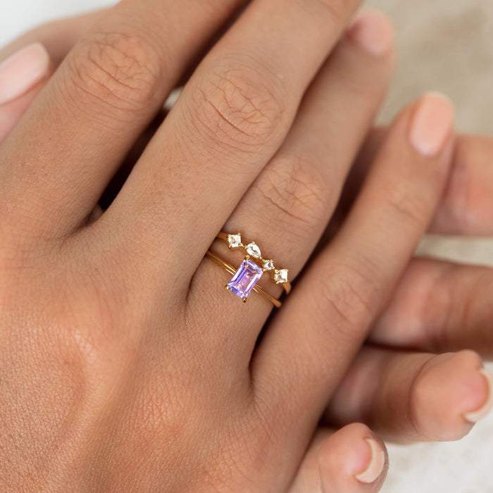 Close-up of a hand wearing Baguette Ring Amethyst - Charlotte with a gold band and rectangular purple gemstone