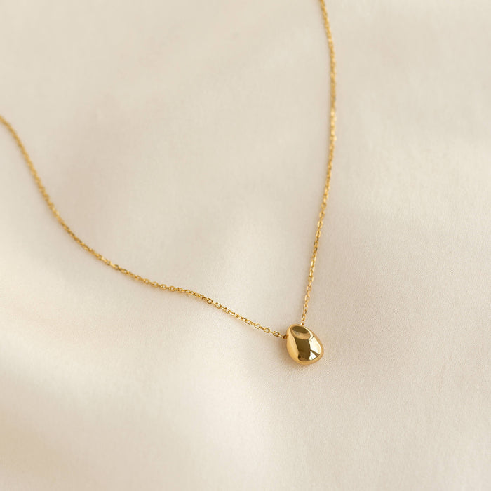 Close-up of Bean Necklace - Karli featuring a sculptural gold vermeil bean pendant on a delicate chain on a cream background
