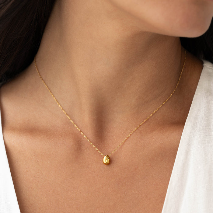 Close-up of a woman wearing the Bean Necklace - Karli with a gold vermeil pendant on a delicate chain and white top