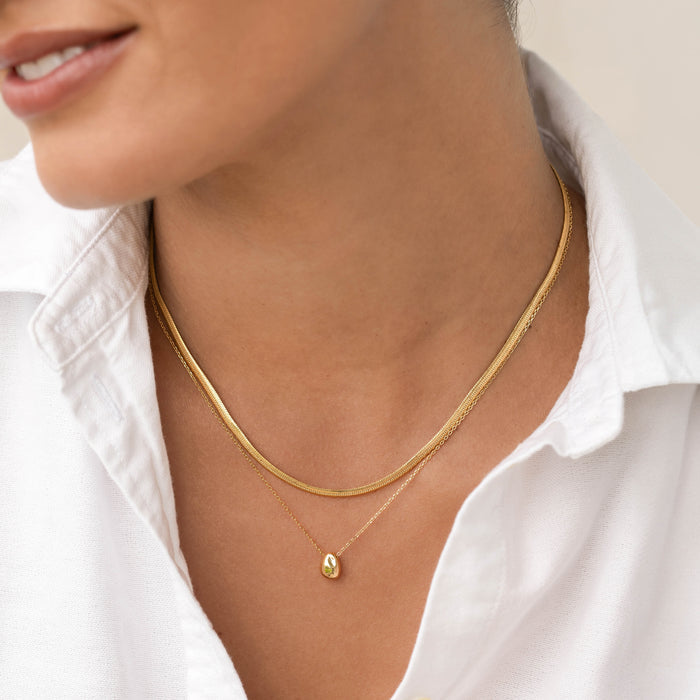 Close-up of a woman wearing the Bean Necklace - Karli with a gold pendant on a delicate chain and white shirt collar visible