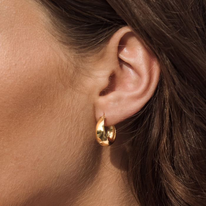 Gold hoop earring worn by a person with brown hair.