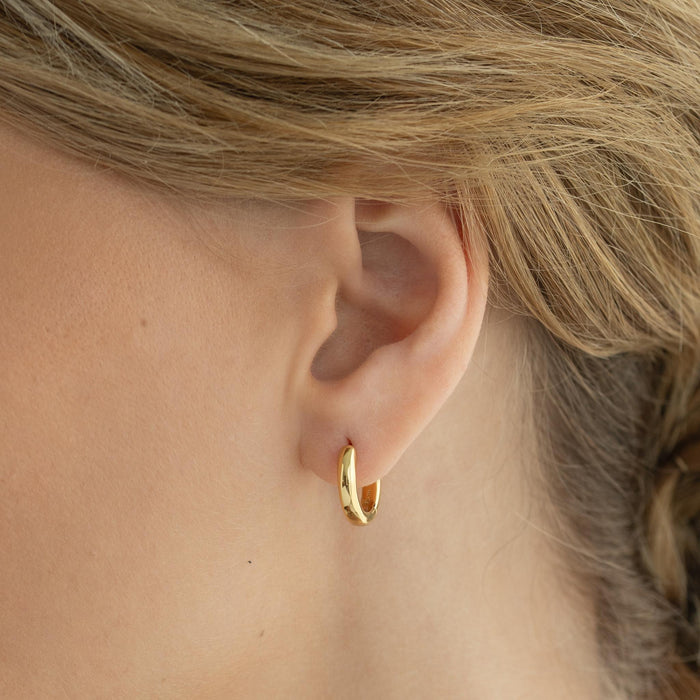 Close-up of a woman wearing Chunky Huggie Hoop Earrings -  Dione crafted in gold vermeil on a neutral background