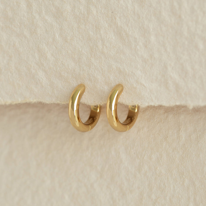 Chunky Huggie Hoop Earrings - Dione in gold vermeil displayed on soft beige textured background