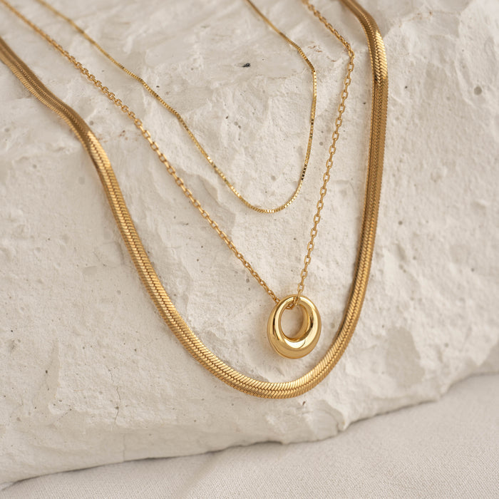 Close-up of gold vermeil layered necklaces featuring the Circle Pendant Necklace - Lilou with a tapered circle pendant on a stone surface