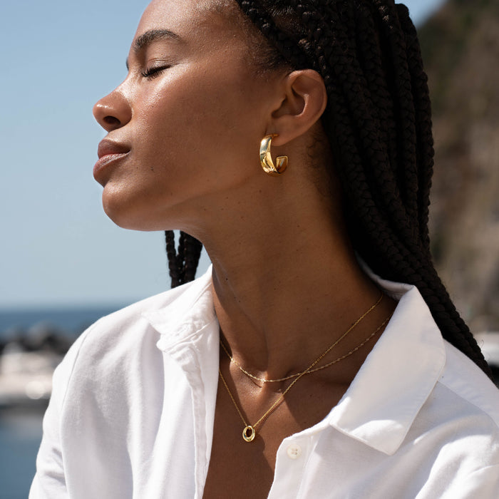 Close-up of woman wearing a gold Circle Pendant Necklace - Lilou and gold hoop earrings against a sunny outdoor background