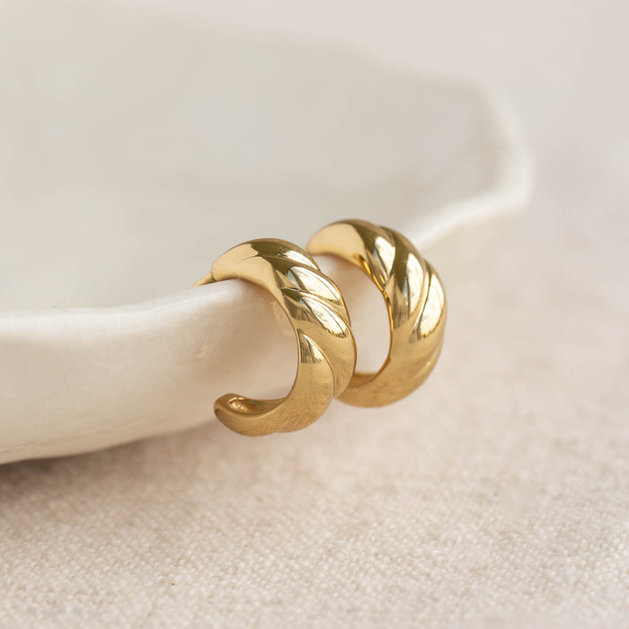Close-up of gold vermeil Croissant Earrings - Piper with a polished twisted design resting on a white ceramic dish