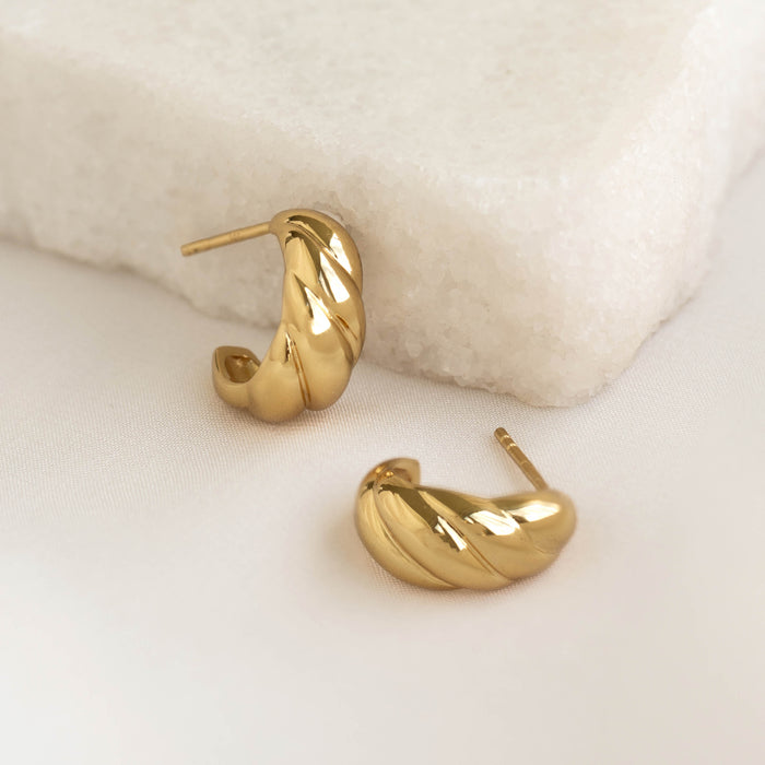 Close-up of gold vermeil Croissant Earrings - Piper with a twisted design on a soft beige fabric background
