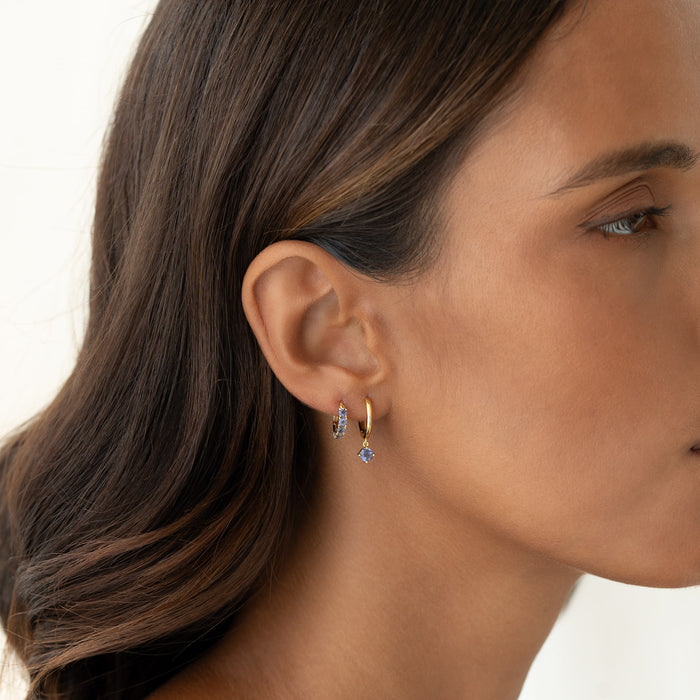 Close-up of a woman wearing December Birthstone Huggie Earrings - Cordierite with gold vermeil setting on a white background