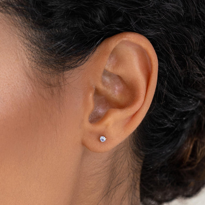 Close-up of an ear wearing December Birthstone Stud Earrings 14k Gold - Tanzanite on a neutral background