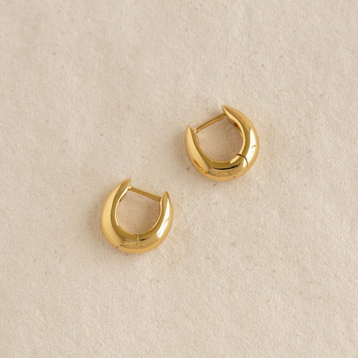 Close-up of Dome Huggie Earrings - Caja in polished gold vermeil with tapered dome shape on a neutral background