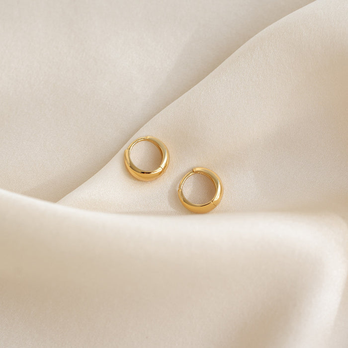 Close-up of gold vermeil Dome Huggie Earrings - Cassia resting on soft cream fabric background