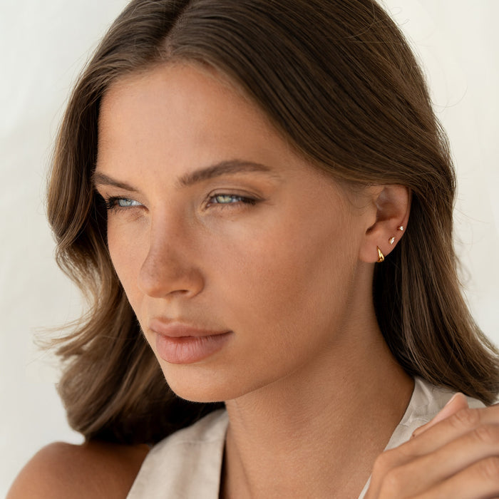 Close-up of a woman wearing Dome Huggie Earrings - Cassia in gold vermeil with three small studs on ear in soft light