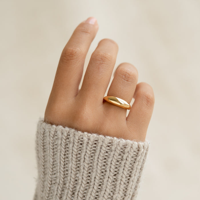 Close-up of a hand wearing the gold Dome Ring - Arielle with a puffy tapered design against a neutral background