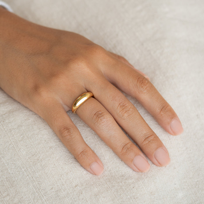 Close-up of hand wearing a gold vermeil Dome Ring - Arielle with a puffy tapered design on a neutral fabric background