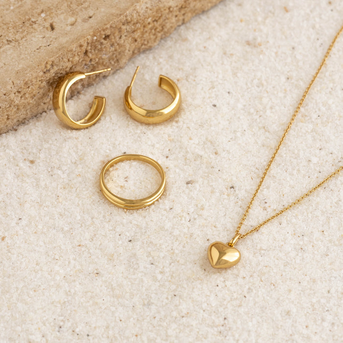 Close-up of gold vermeil Double Stacking Ring - Idalia with matching gold hoop earrings and heart pendant necklace on sandy surface