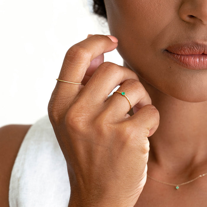 Close-up of a woman wearing the Emerald Ring 14k Gold - Penelope with a simple gold band on a white top