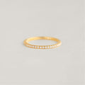 A delicate Gold band ring with small diamonds encircling it is placed on a soft, neutral background, exuding elegance and simplicity.