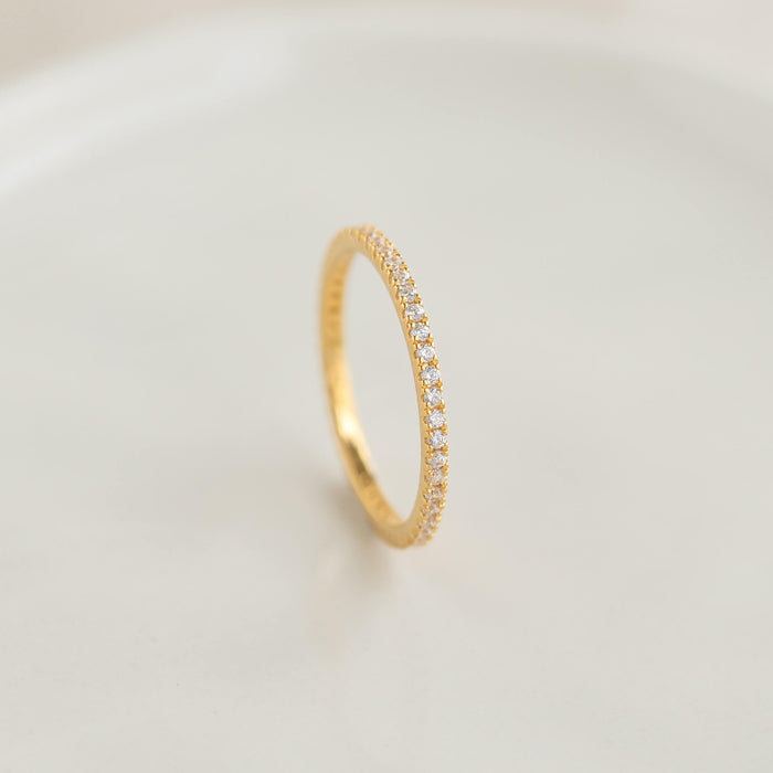 A delicate Gold ring adorned with small diamonds, set against a soft, neutral background. The ring conveys elegance and simplicity.