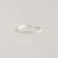 A delicate White Gold eternity ring adorned with small diamonds, elegantly placed on a soft, light gray surface, conveying a sense of simplicity and elegance.
