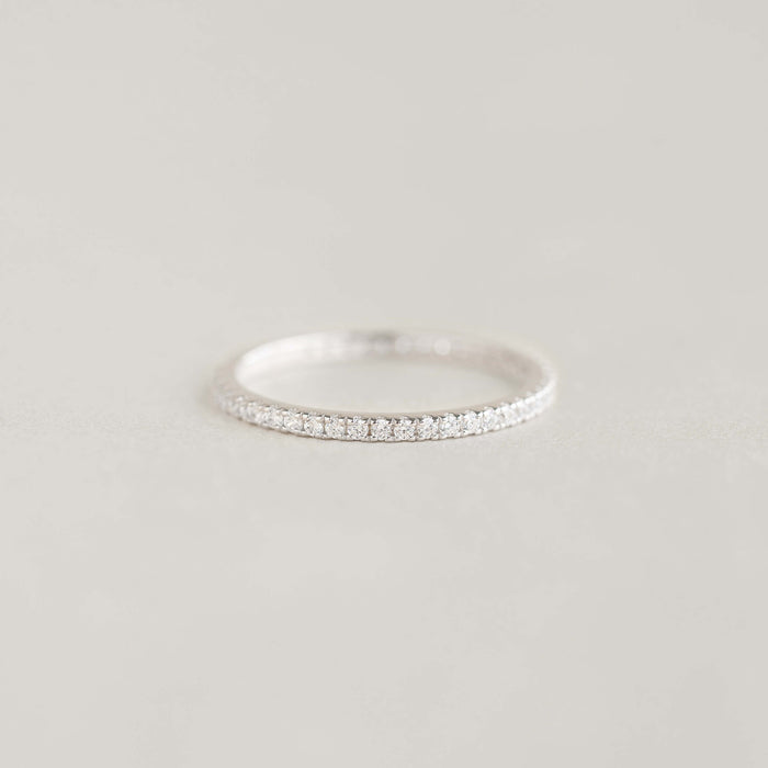 A delicate White Gold eternity ring adorned with small diamonds, elegantly placed on a soft, light gray surface, conveying a sense of simplicity and elegance.