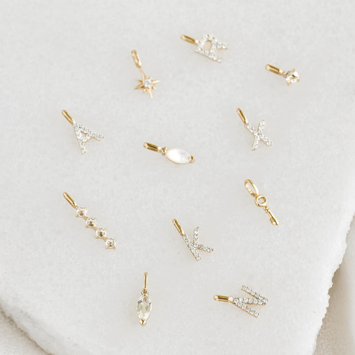 Four Leaf Clover Charm 14k Gold displayed with other delicate gold initial and gemstone charms on a neutral background