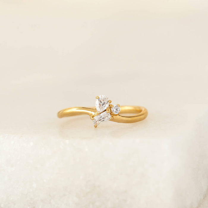 Delicate Gold Vermeil ring featuring a cluster of mixed-cut gemstone, including pear, round, and baguette shapes, set on a slim band and displayed on a soft neutral surface.