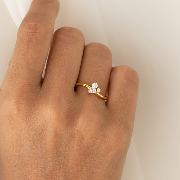 Close-up of a hand wearing a delicate Gold Vermeil ring with a curved band, featuring a cluster of mixed-cut gemstone including pear, round, and baguette shapes.