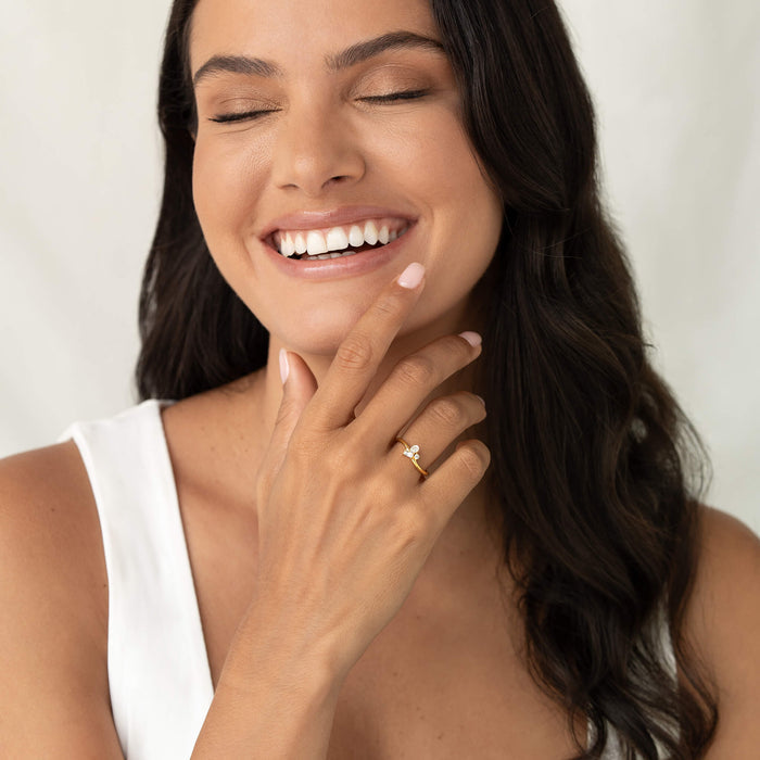 Smiling woman with eyes closed wearing a delicate Gold Vermeil ring featuring a cluster of mixed-cut gemstone, shown on her hand as she gently touches her face against a soft neutral background.