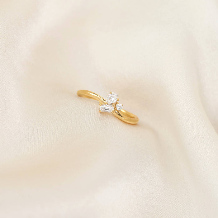 Delicate Gold Vermeil ring with a slim band, featuring a cluster of mixed-cut gemstone including pear, round, and baguette shapes, placed on softly draped ivory fabric.