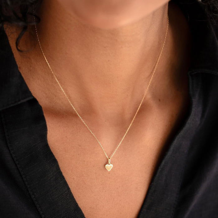 Close-up of a woman wearing the Heart Charm 14k Gold necklace with a delicate beaded border on a black top