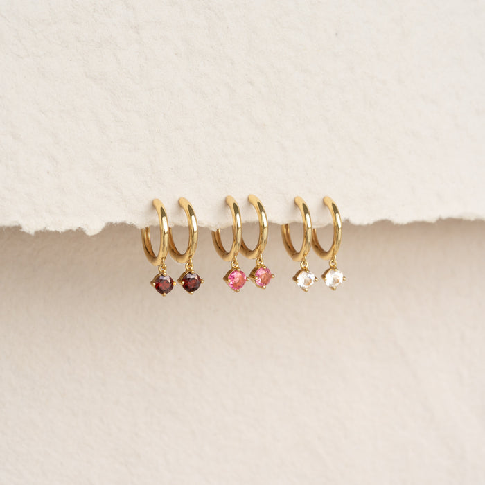 Close-up of January Birthstone Drop Huggie Earrings - Garnet with gold vermeil and red gemstones on a neutral background