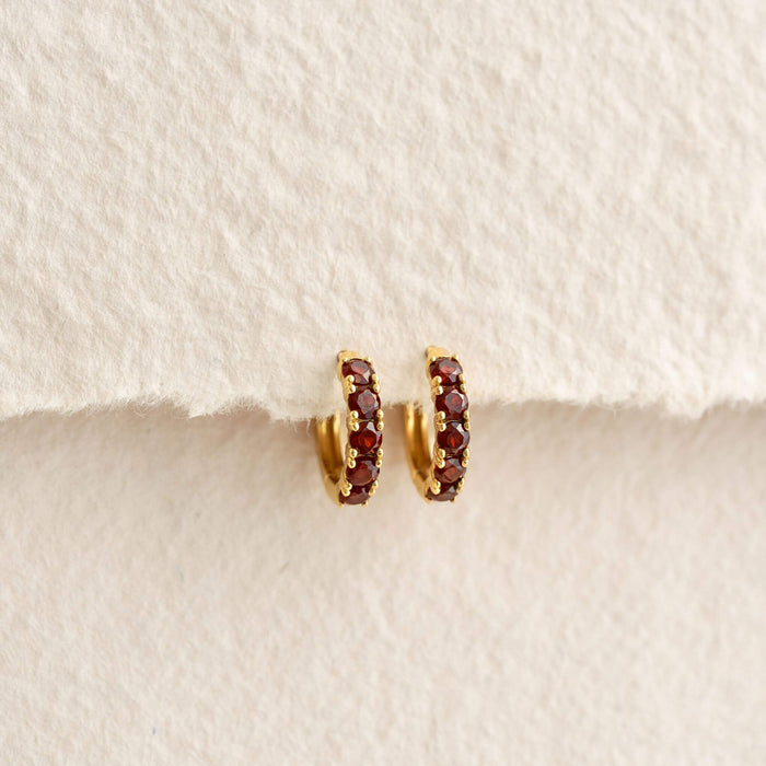 January Birthstone Huggie Earrings - Garnet featuring small garnet stones set in gold vermeil on a cream background