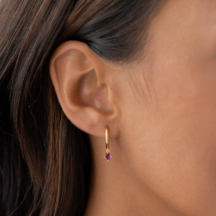 Close-up of an ear wearing July Birthstone Drop Huggie Earrings - Pink Tourmaline with gold vermeil setting