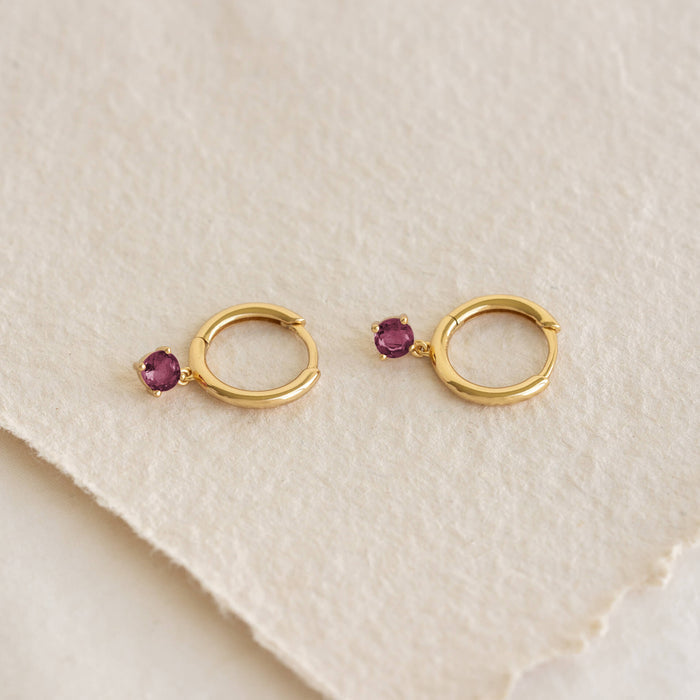 Close-up of July Birthstone Drop Huggie Earrings - Pink Tourmaline featuring gold vermeil hoops with pink gemstones on textured background
