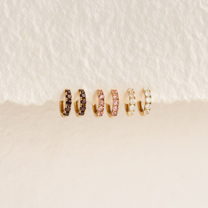 Six pairs of June Birthstone Huggie Earrings - Moonstone in gold vermeil displayed on textured white surface