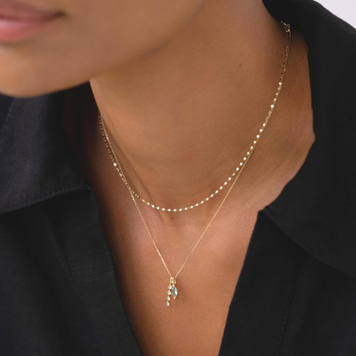 Close-up of woman wearing Diamond Drop Pendant 14k Gold layered with a delicate beaded 14k gold chain on black top