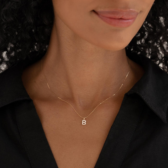 Close-up of woman wearing Diamond Initial Pendant 14k Gold - B on delicate gold chain with black collared shirt