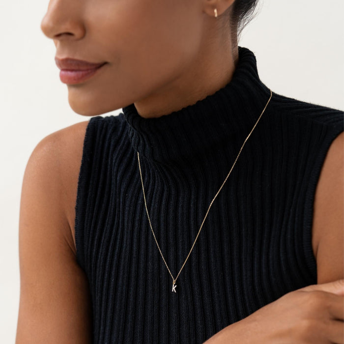 Close-up of a woman wearing a Diamond Initial Pendant 14k Gold - K on a delicate gold chain with a black ribbed turtleneck