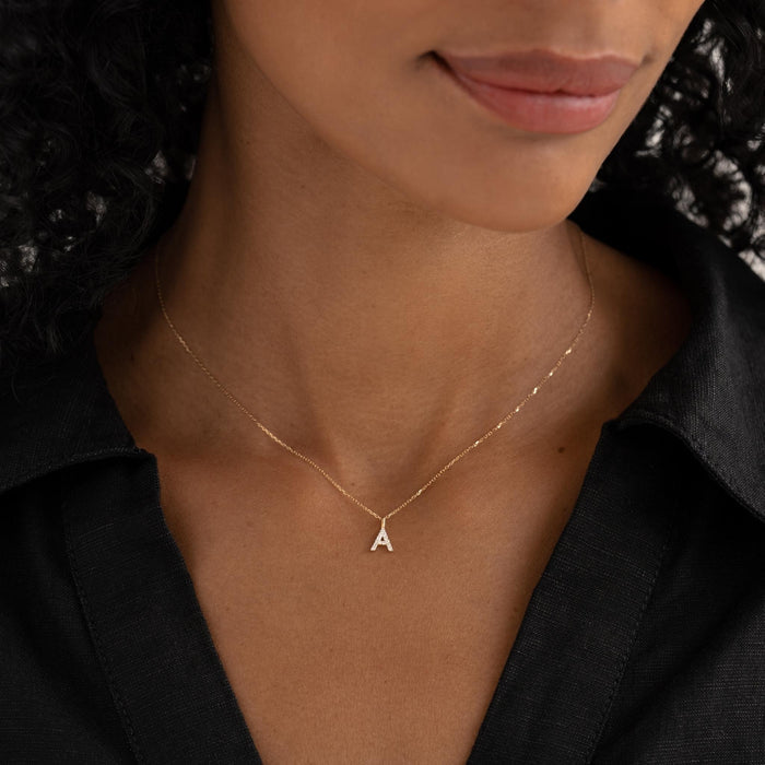 Close-up of a woman wearing Diamond Initial Pendant 14k Gold - O on a delicate gold chain with a black collared shirt