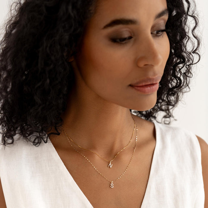 Close-up of a woman wearing the Diamond Initial Pendant 14k Gold - R styled with a white sleeveless top