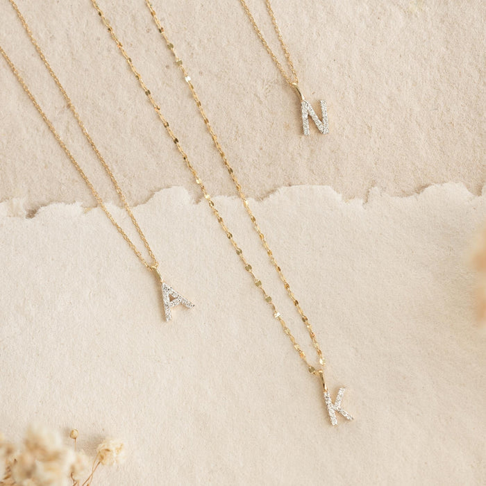 Diamond Initial Pendant 14k Gold - V styled with other letter pendants A, K, and N on gold chains on a neutral background
