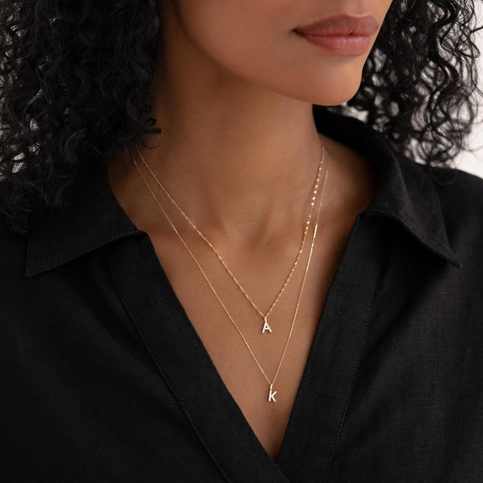 Close-up of woman wearing layered Diamond Initial Pendant 14k Gold - V with other letter pendants on black top